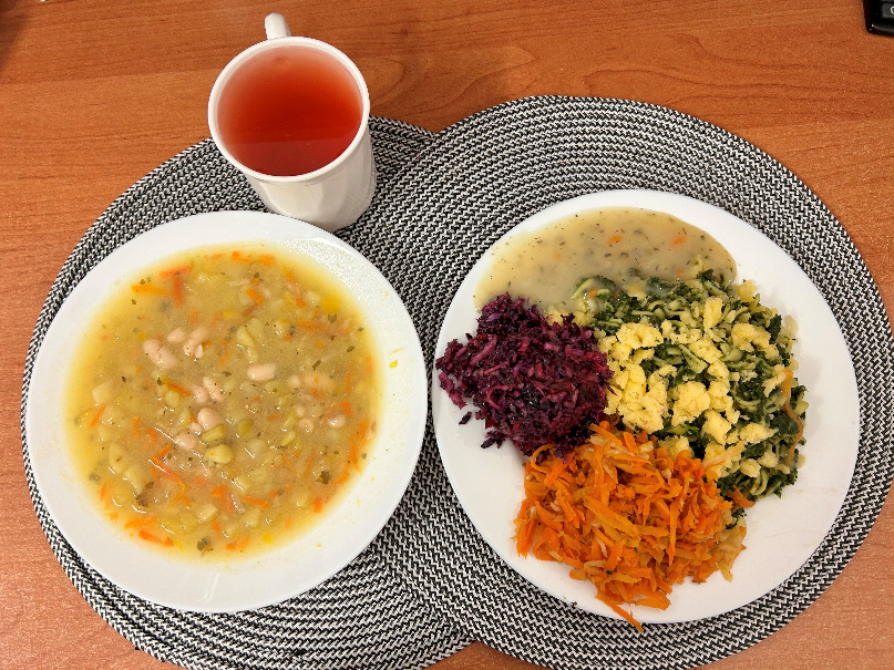 Na zdjęciu znajduje się: Fasolowa z ziemniakami 400 ml (GLU PSZ, SEL) Makaron ze szpinakiem i serem żółtym 350 g (GLU PSZ, MLE) Sos bazyliowy, Sałatka z kapusty czerwonej z olejem, Bukiet jarzyn gotowany z olejem, Kompot owocowy